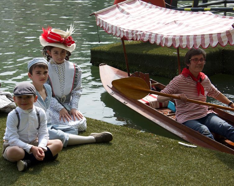 3 petits enfants costumés sont assis par terre sur le quai à côté de la périssoire