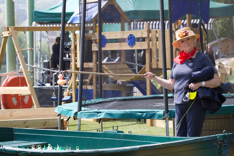 Une dame avec un canotier montre un canard en plastique au bout d'une canne à pêche